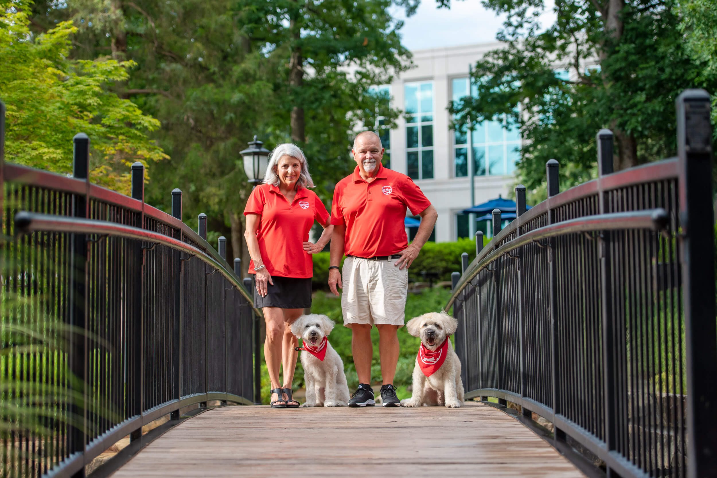 Off Leash Dog Training co-owners Jan and Russ standing on bridge with their two dogs in Charlotte, NC